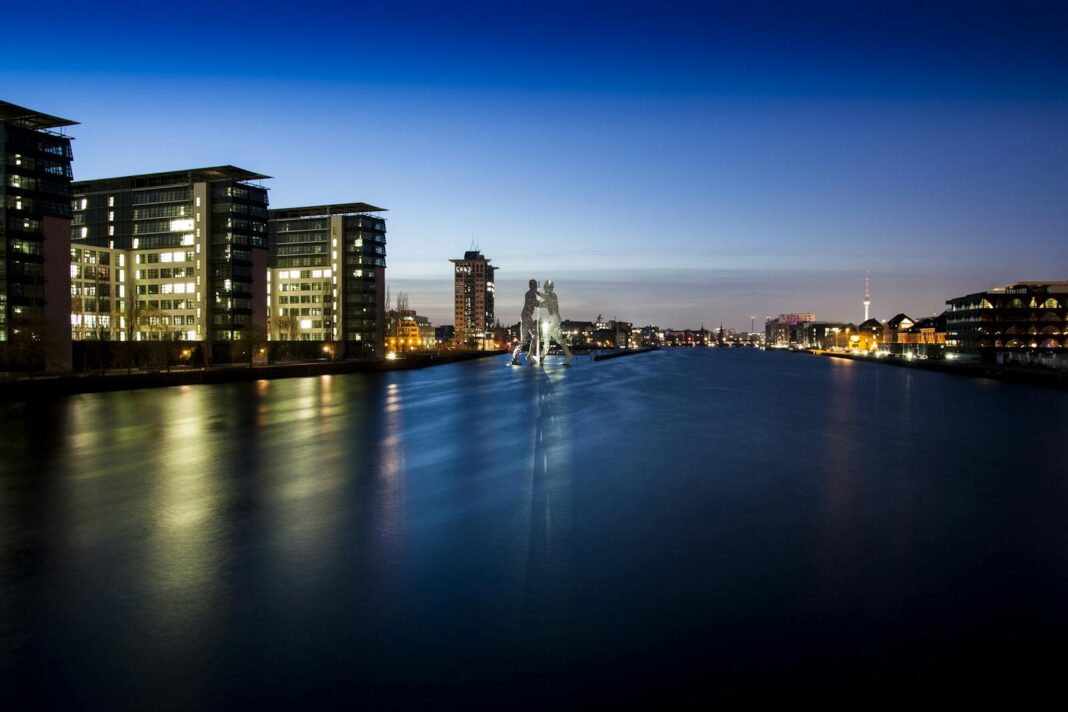 Night view of Berlin's skyline featuring the iconic Molecule Man sculpture along the Spree River.