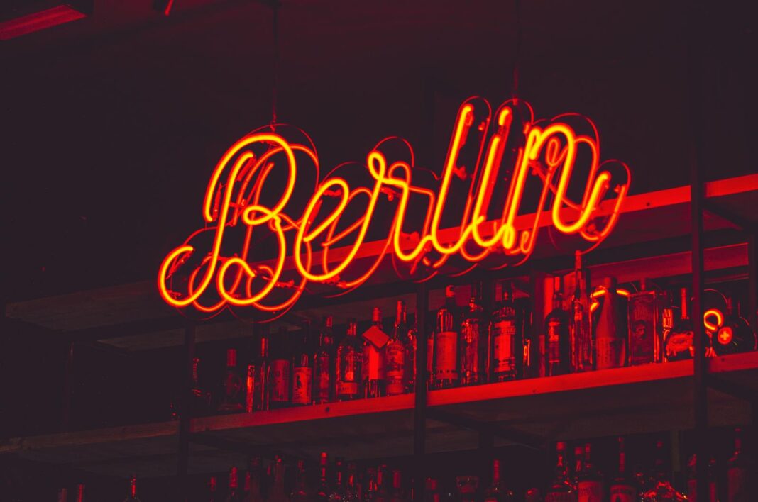 Illuminated Berlin neon sign above a shelf of alcohol bottles in a bar setting.